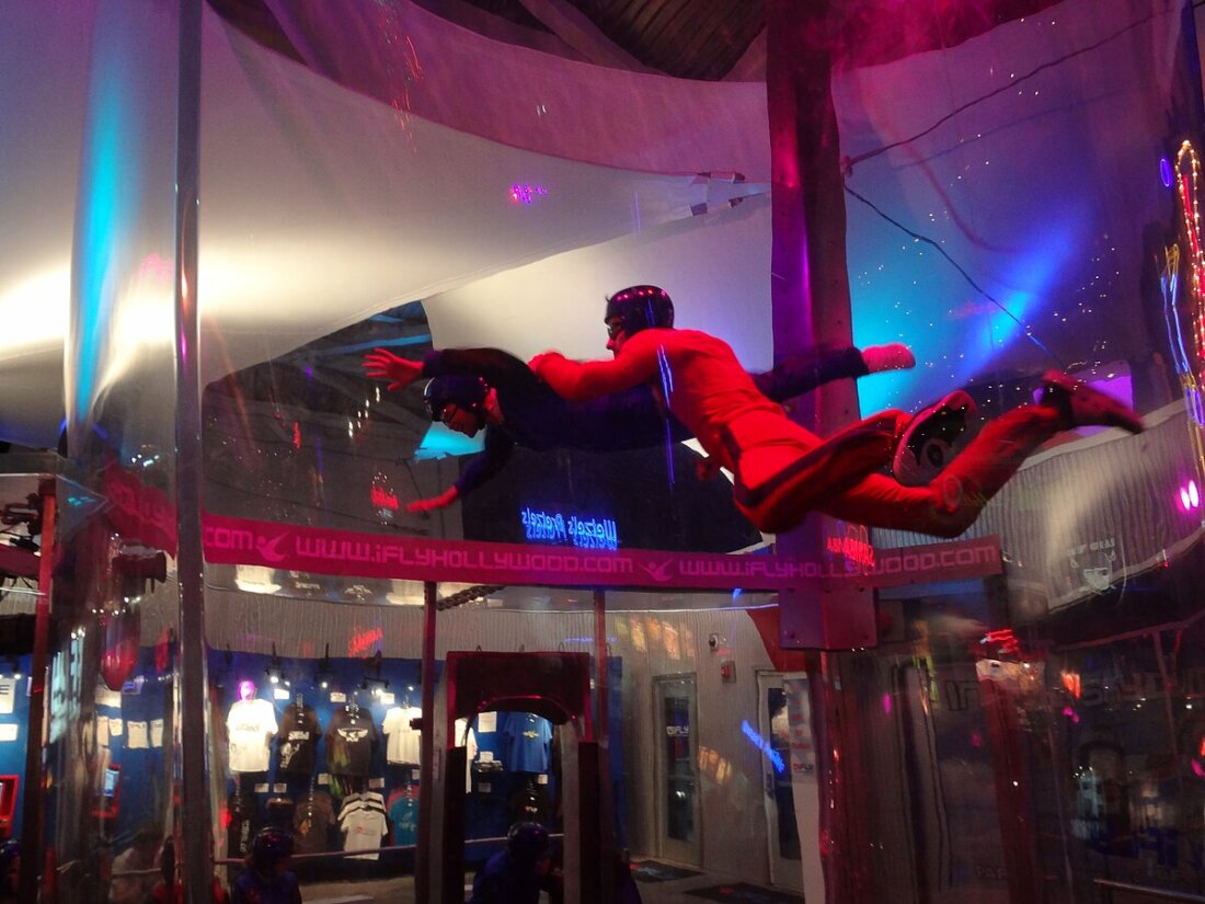 Skydiver in red suit suspended in indoor wind tunnel, practicing skydiving skills.