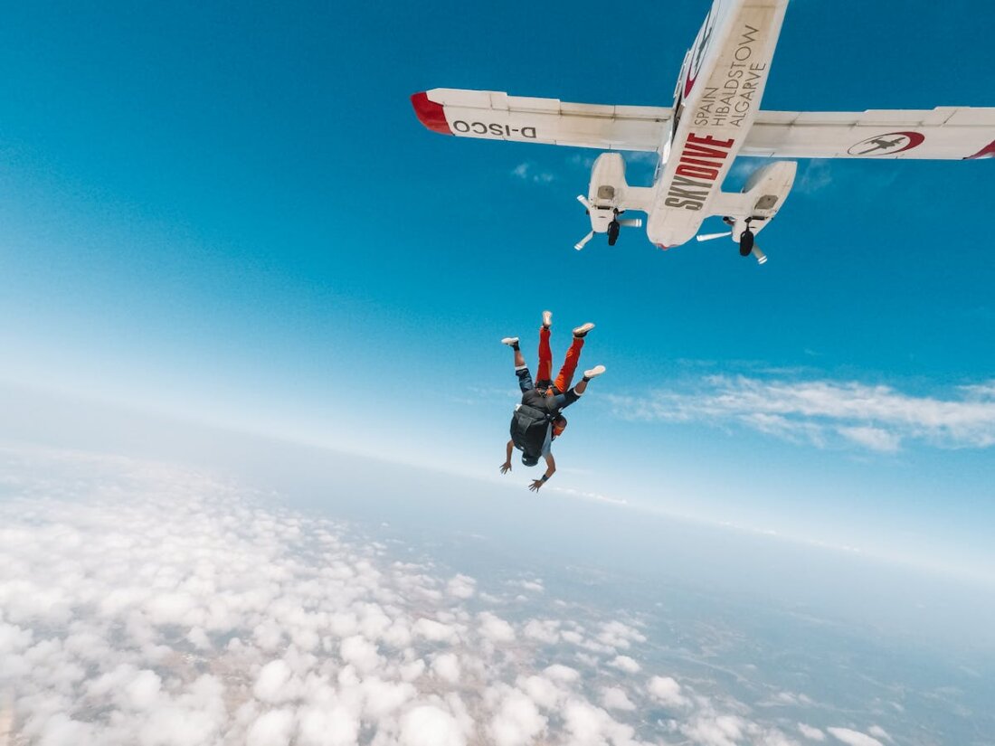 Two skydivers in freefall exiting a plane above the clouds