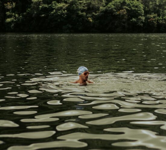 Schwimmer mit Badekappe beim Freiwasserschwimmen in einem ruhigen Waldsee