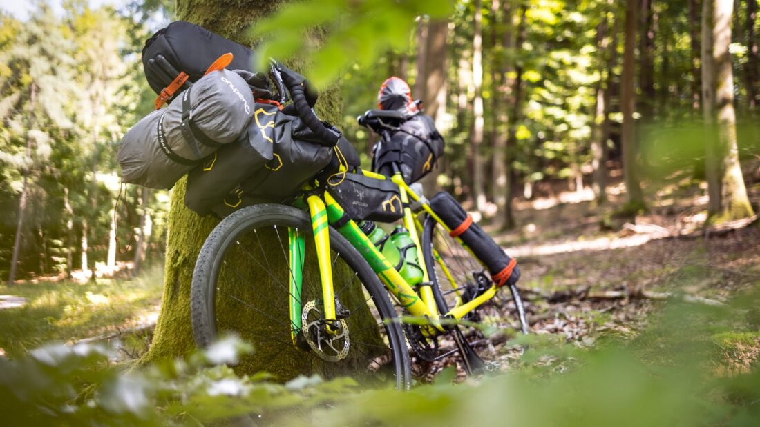 Bikepacking-Gravel-Rad mit Lenker-Roll und Rahmentasche im Wald