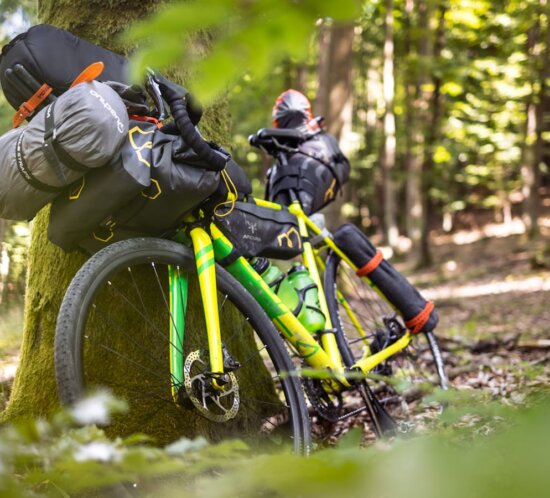 Bikepacking-Gravel-Rad mit Lenker-Roll und Rahmentasche im Wald