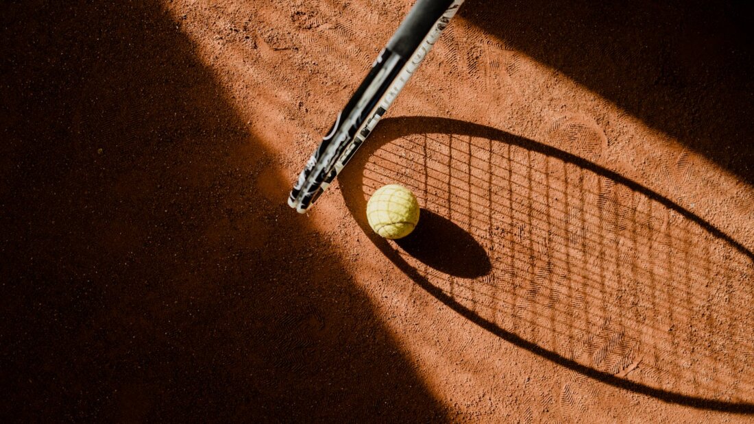 Tennisball auf rotem Sandplatz mit Schläger-Schatten, Symbolbild zur Sandplatz-Saison bei Roland Garros