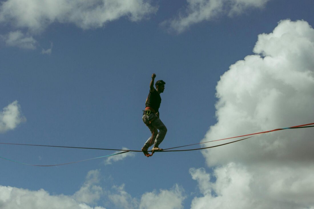 Sportler balanciert konzentriert auf einer Slackline gegen blauen Himmel, ein Arm zum Ausgleich erhoben.