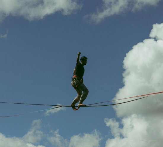 Sportler balanciert konzentriert auf einer Slackline gegen blauen Himmel, ein Arm zum Ausgleich erhoben.
