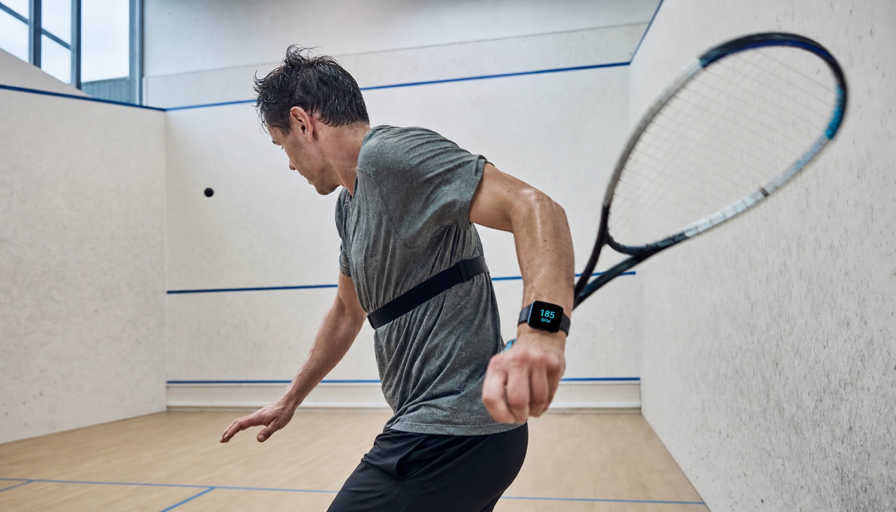Ein Squash-Spieler in vollem Einsatz, während ein Pulsmessgerät eine hohe Herzfrequenz anzeigt - Symbol für die intensive Belastung im engen Court.