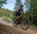 Eine Mountainbikerin fährt auf einem Mountainbike über einen staubigen Waldtrail zwischen dichtem Baumbestand.