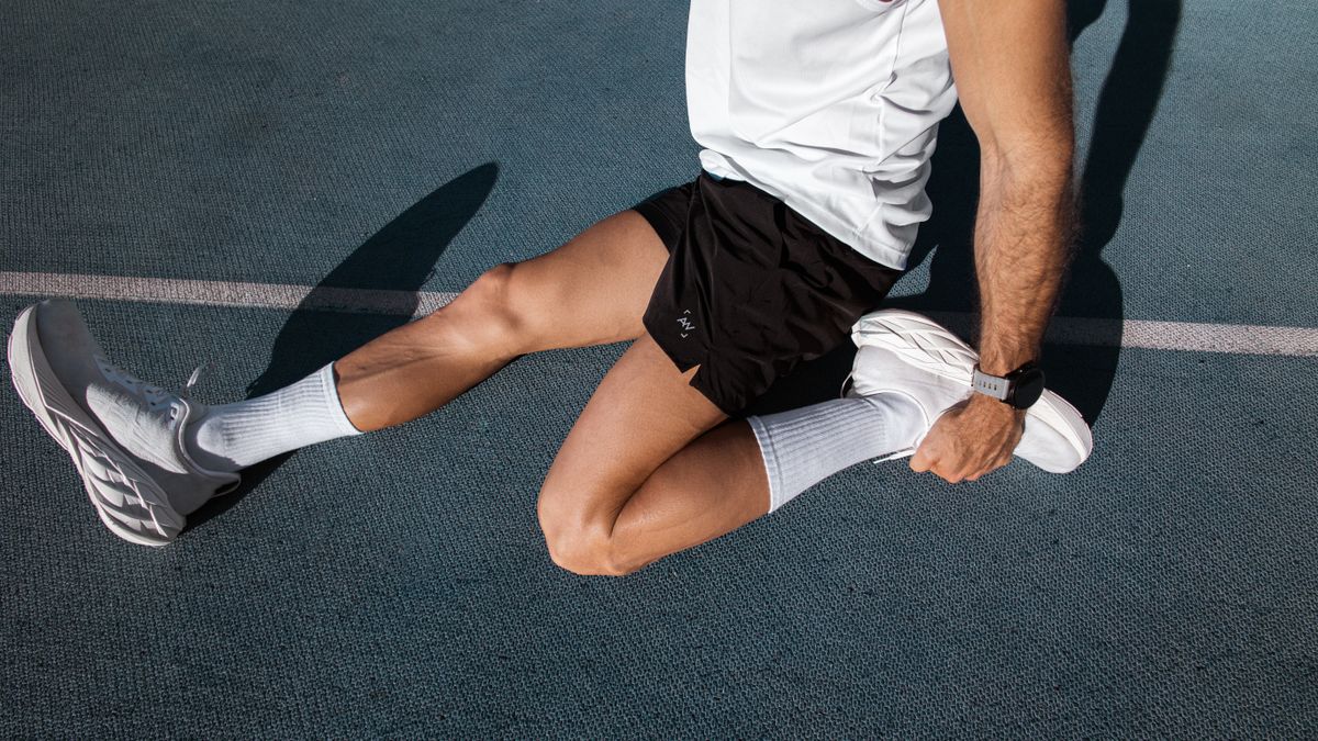 Läufer dehnt nach dem Training auf der Bahn, Fokus auf Beine und Laufschuhe