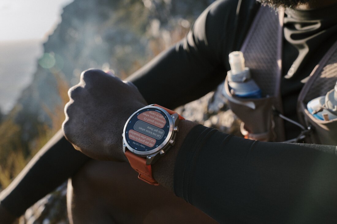 Garmin Fenix 9 Pro mit orangem Armband am Handgelenk eines Trailläufers, im Hintergrund Felsen und Morgenlicht (Pressebild Garmin)