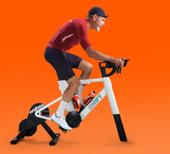 Fahrer auf dem Zwift Ride V2 mit Wahoo Kickr Core vor oranger Fläche (Pressebild Zwift)